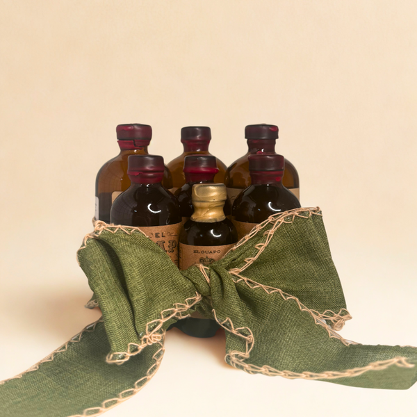 Collection of 4 bitters and 3 syrups for bourbon pairings tied with a green bow on a butter yellow background