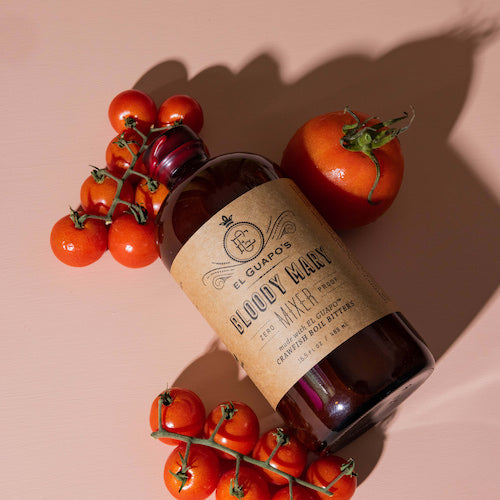 Bottle of 'El Guapo Bloody Mary' with tomatoes on a pink background