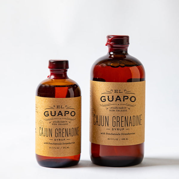 Size comparison of a large and small bottle of El Guapo Cajun Grenadine syrup on a white background