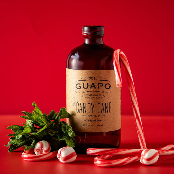 Bottle of El Guapo Candy Cane Syrup with candy canes and mint leaves on a red background