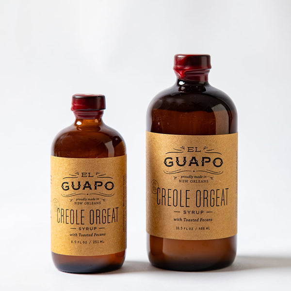 Size comparison of two bottles of El Guapo Creole Orgeat syrup on a white background