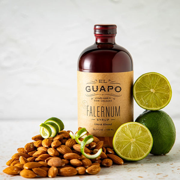Large bottle of El Guapo Falernum syrup with limes and almonds on a light background