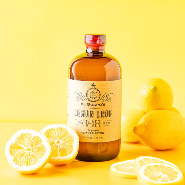 Bottle of El Guapo Lemon Drop Mixer with lemons on a yellow background