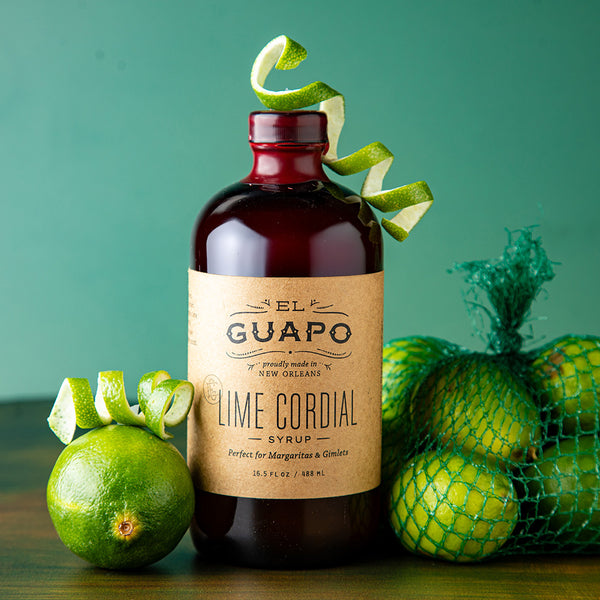 Bottle of large 16.5 oz bottle El Guapo Lime Cordial Syrup with limes on a green background