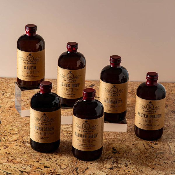 Set of six assorted El Guapo Mixers bottles arranged on a cork surface