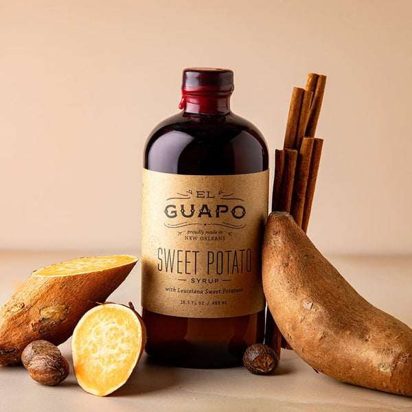 Bottle of Guapo Sweet Potato Syrup with sweet potatoes and cinnamon sticks on a beige background