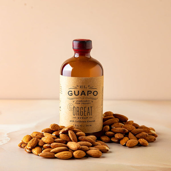 Bottle of small 16.5 oz El Guapo Orgeat Syrup with almonds on a beige background