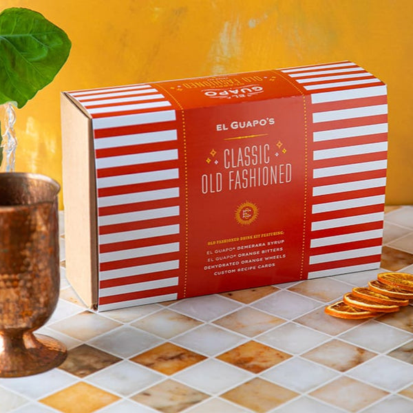 Orange and white striped box with 'El Guapo's Classic Old Fashioned' on a tiled surface.