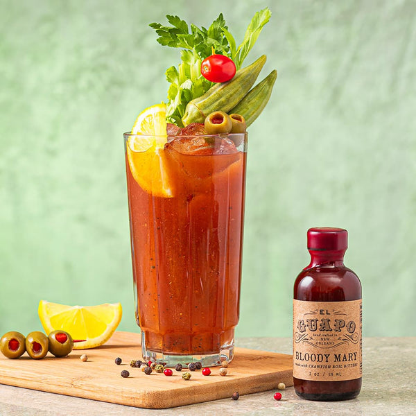 Bloody Mary cocktail with garnishes and a single serving bottle of El Guapo Bloody Mary Mixer on a wooden board.