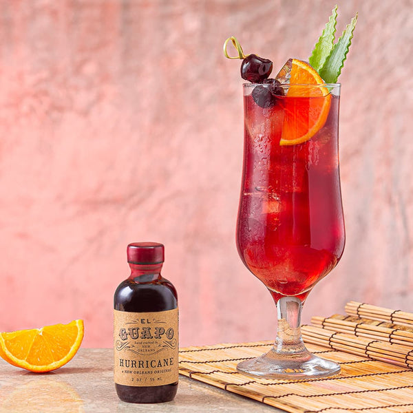 Cocktail with garnishes and a single serving bottle of El Guapo Hurricane Mixer on a bamboo mat.