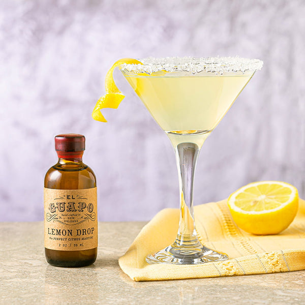Sugar Rimmed Lemon Drop Martini with a bottle of Single Serving Guapo Lemon Drop Mixer on a wooden surface.