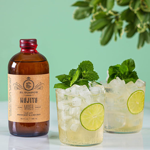 El Guapo Mojito Mixer bottle with two glasses of mojitos garnished with lime wheels and mint leaves on a light green background.