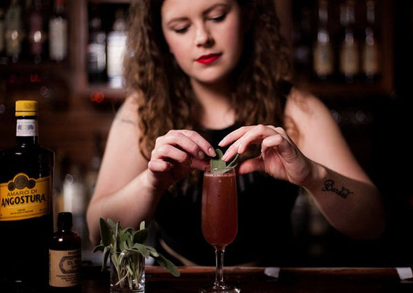 A bartender garnishing a cocktail with fresh sage next to Amaro di Angostura