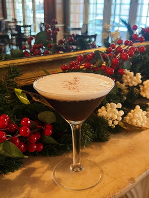 The Merry Christa holiday martini with a foam top next to festive winter greenery