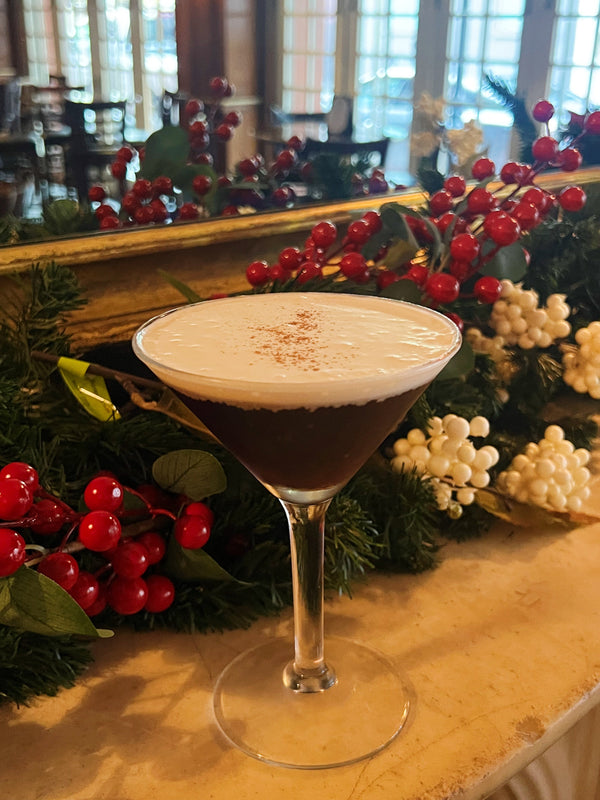 The Merry Christa holiday martini with a foam top next to festive winter greenery