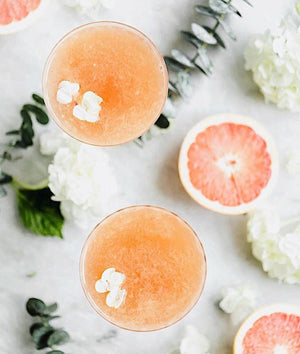 Top-down view of Polynesian Paloma grapefruit cocktails with fresh sliced citrus and white flowers