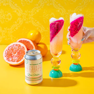 Two tropical dragon fruit cocktails next to an El Guapo Love Potion Bitters & Soda can