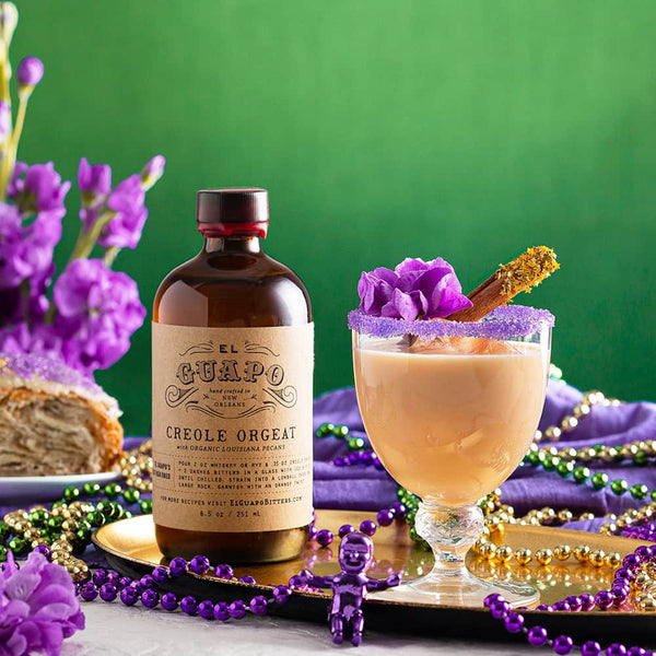 King Cake Cocktail with purple sugar rim next to El Guapo Creole Orgeat