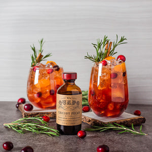 Thanksgiving cocktails garnished with rosemary next to El Guapo Chicory Pecan Bitters