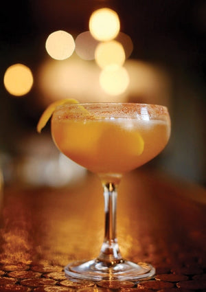 Foster The People cocktail with a spiced rim and lemon twist on a bar counter