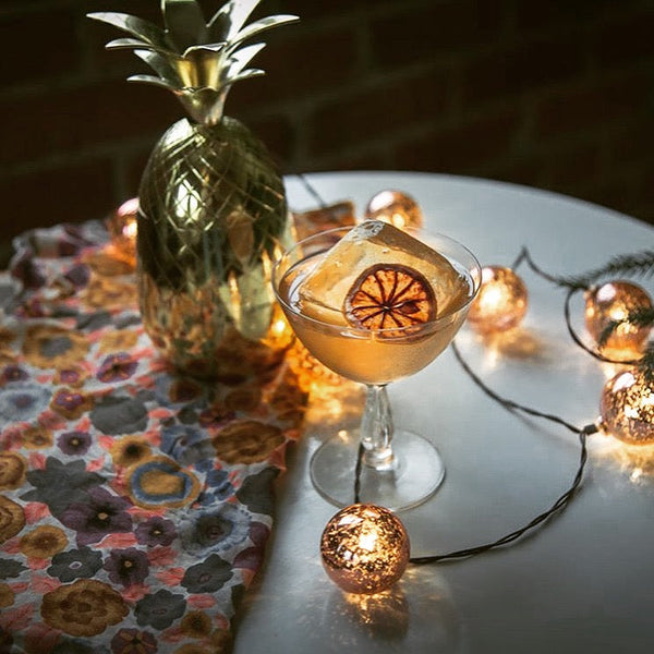 Craft cocktail with a dried citrus wheel garnish, a gold pineapple, and festive string lights