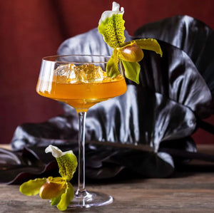 Tropical Salted Caramel-tini with ice in a coupe glass garnished with a yellow orchid