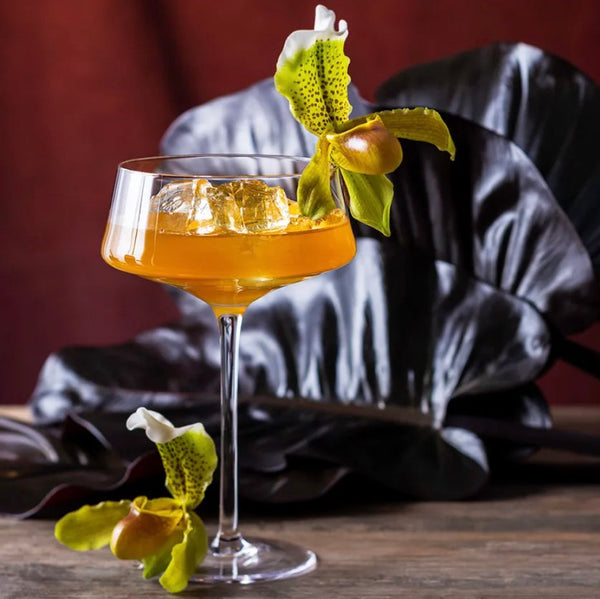 Tropical Salted Caramel-tini with ice in a coupe glass garnished with a yellow orchid