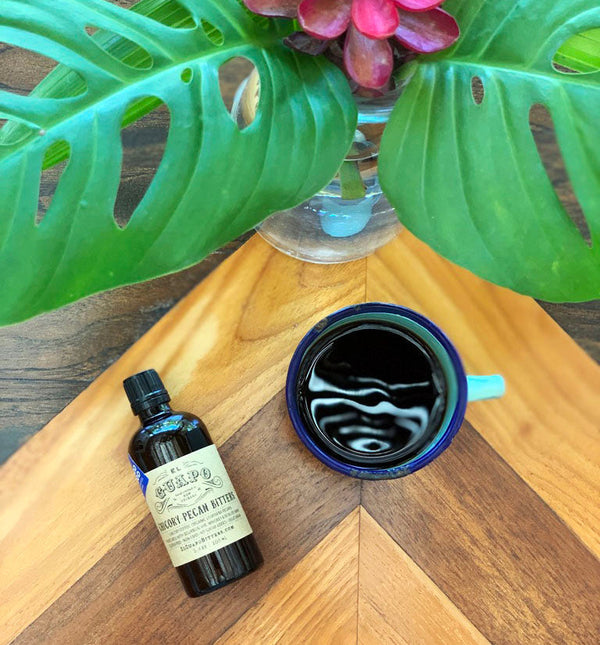 Black coffee in a blue mug next to a bottle of El Guapo Chicory Pecan Bitters
