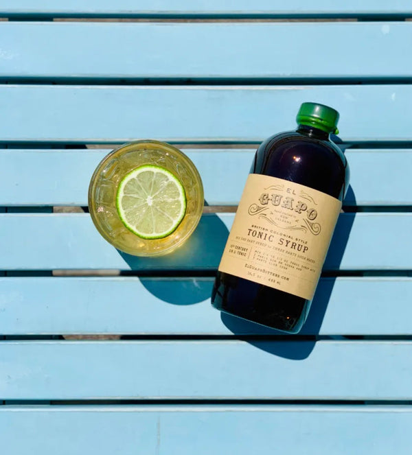 Tonic water with a lime wheel garnish next to a bottle of El Guapo Tonic Syrup