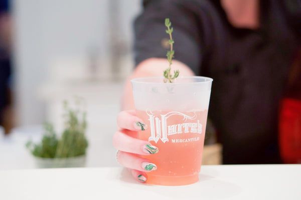 Pink cocktail garnished with herb sprig in a White's Mercantile cup