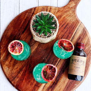 Cuban Daze turquoise cocktails with blood orange wheels next to El Guapo Cuban Bitters
