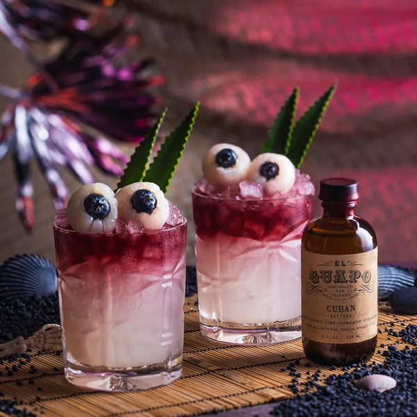Freaky Tiki cocktails with lychee eyeball garnishes next to a bottle of El Guapo Cuban Bitters