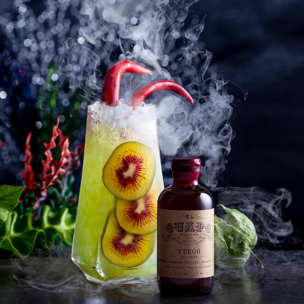 Smoking green kiwi cocktail with red pepper garnish next to El Guapo Fuego Bitters