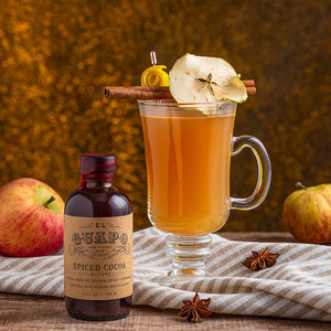 Spiked Hot Cider with a cinnamon stick garnish next to El Guapo Spiced Cocoa Bitters