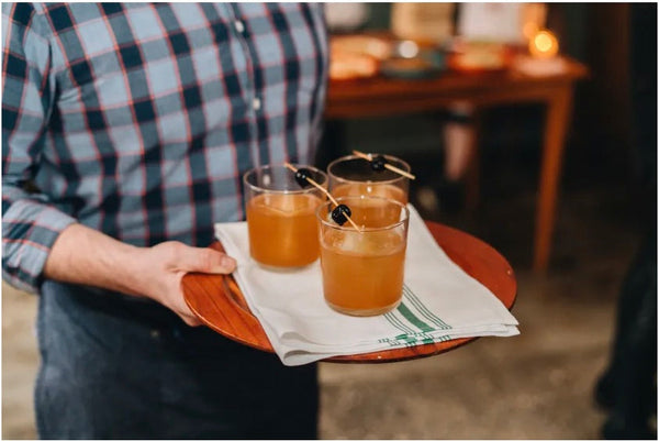 Server carrying a tray of Black Old Fashioned cocktails garnished with cherries