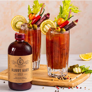 Bloody Mary cocktails with celery and pepper garnishes next to El Guapo Bloody Mary Mix