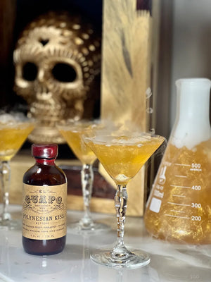 Hocus Pocus glitter cocktail with dry ice next to a bottle of El Guapo Polynesian Kiss Bitters