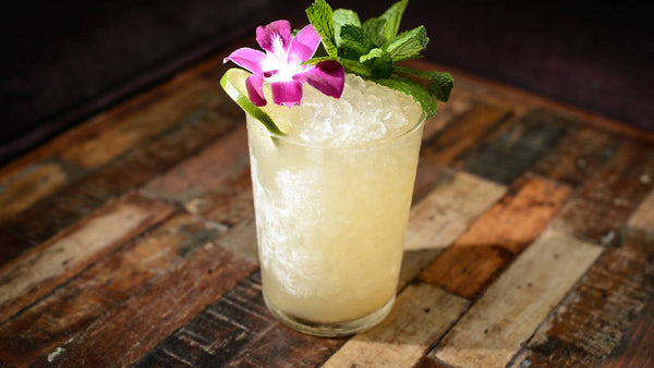 Mai Tai cocktail with crushed ice, fresh mint, and an orchid flower on a wooden table