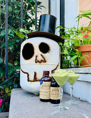 Green frozen martinis next to a decorative skeleton and El Guapo Bitters bottles