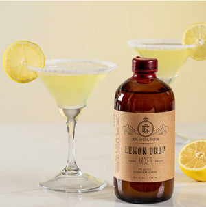 Lemon Drop Martini with a sugar rim and lemon wheel next to a bottle of El Guapo Lemon Drop Mixer