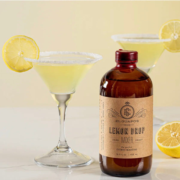 Lemon Drop Martini with a sugar rim and lemon wheel next to a bottle of El Guapo Lemon Drop Mixer
