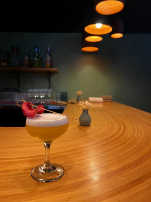 Lengua Milk Punch cocktail on a curved wooden bar counter under warm hanging lights