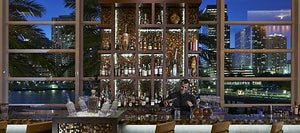 A bartender mixing a lavender gin martini at an upscale bar with city views