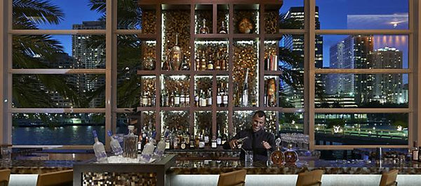 A bartender mixing a lavender gin martini at an upscale bar with city views