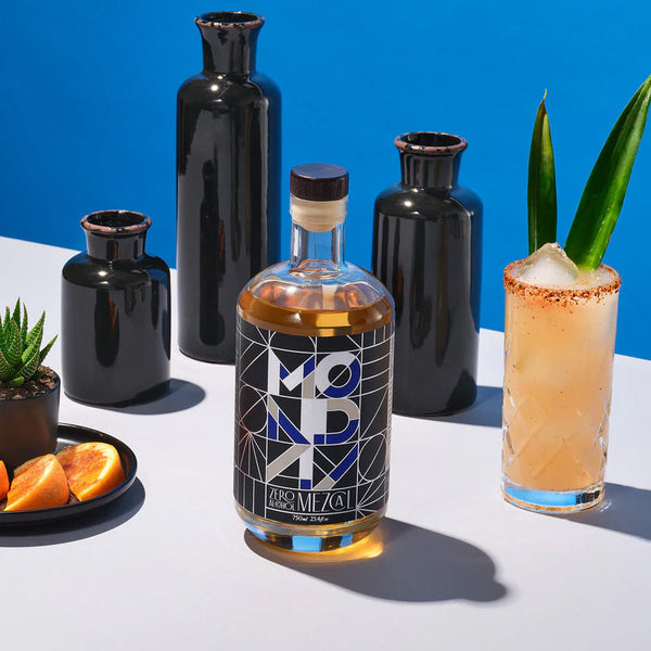 Monday Zero Alcohol Mezcal bottle next to a non-alcoholic Paloma cocktail with a chili rim