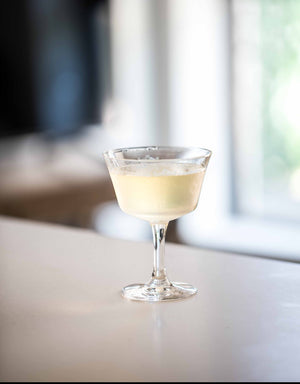 A classic Pisco Sour cocktail served in a coupe glass on a bright white bar counter