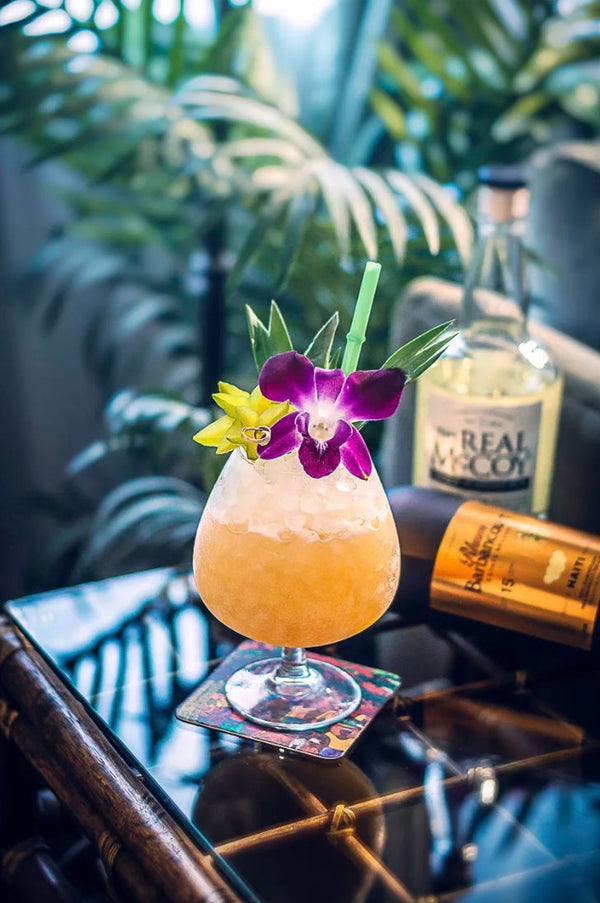 Tropical pineapple lime cocktail garnished with a purple orchid next to bottles of rum