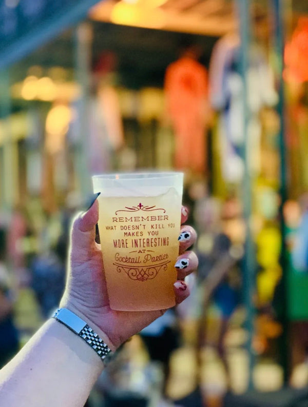 Hand holding a rum party punch cup with a quote against a blurry background