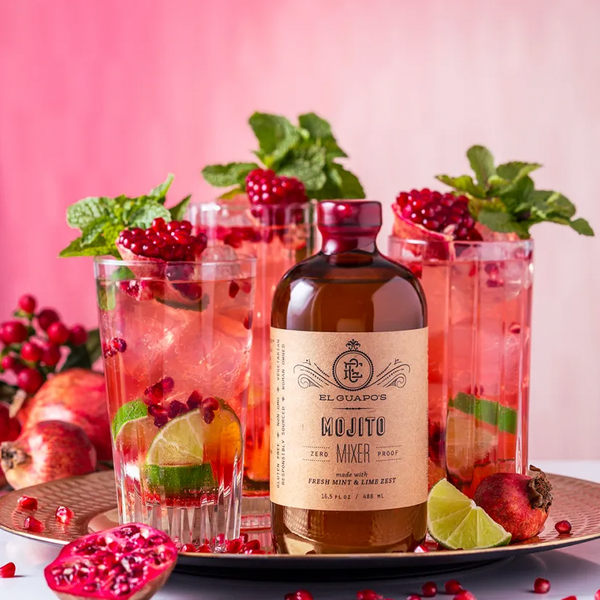 Pomegranate mojitos with fresh mint and limes next to a bottle of El Guapo Mojito Mixer