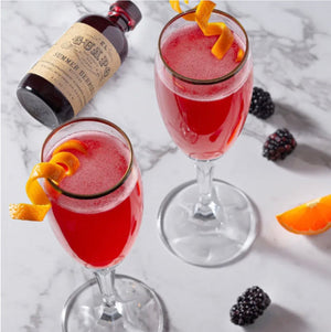 Seasonal French 75 cocktails with orange twists next to El Guapo Summer Berries Bitters